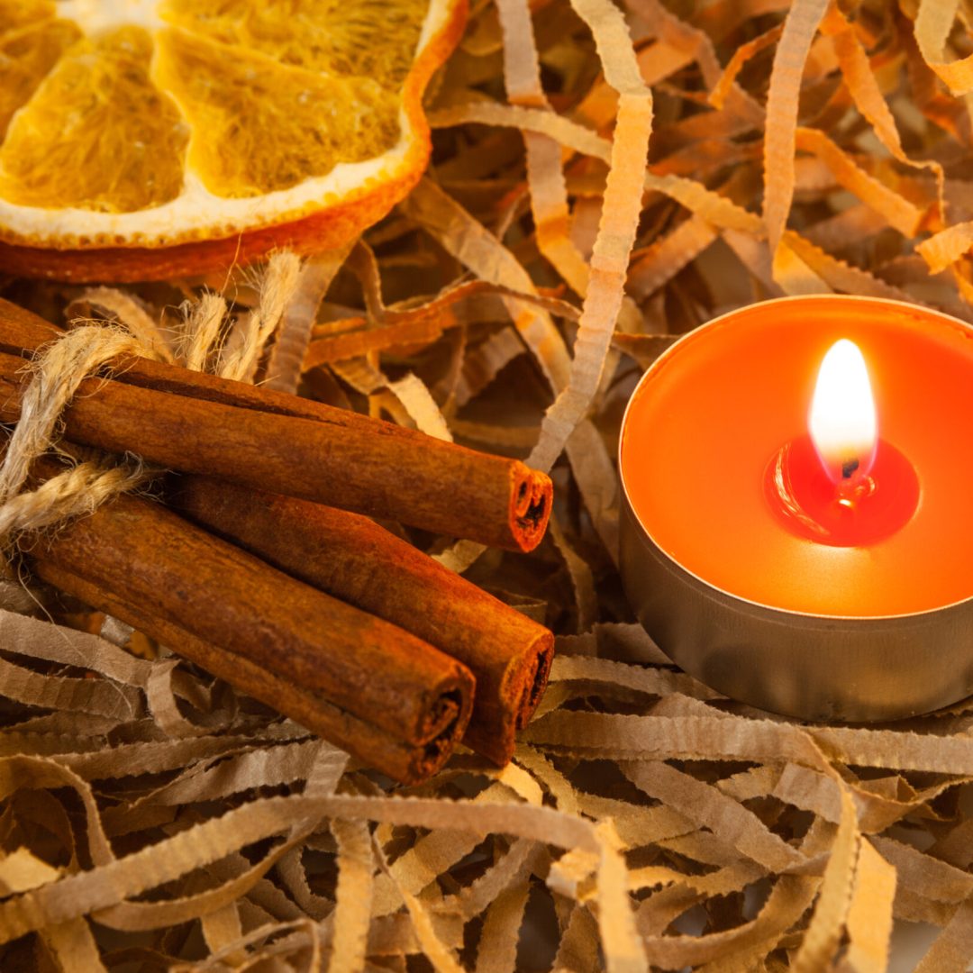 Orange slice and fragrant cinnamon sticks with a red burning candle